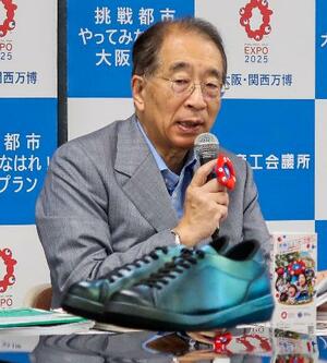 記者会見する大阪商工会議所の鳥井信吾会頭。手前は電磁石の反発を利用した「宙に浮く靴」=18日午後、大阪市中央区