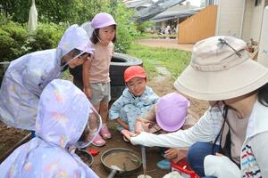 「羽茂こども園」の保育園留学第1号の園児(中央)。園庭でミミズを見つけ、笑顔を見せた=6月、佐渡市羽茂本郷