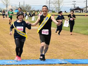 骨髄バンクへの協力を呼びかけるたすきを着けてゴールする古川俊治さん(中央)ら=見附市本町
