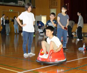 自分で入力したプログラムで動く自動車に乗る子どもたち=佐渡市石田