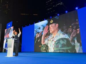 　選挙集会で演説するアヌティン首相。背後の大画面に軍服姿が映し出された＝１月、バンコク（共同）