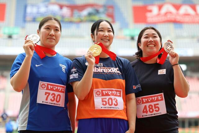 女子円盤投げで優勝した郡菜々佳（サトウ食品新潟アルビレックスＲＣ・中央）。表彰式でメダルを掲げ笑顔を見せる＝デンカビッグスワン