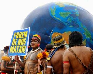 熱帯林保護などを訴え、「私たちを殺すのをやめろ」と書かれたプラカードを掲げる先住民男性=15日、ブラジル・ベレン(共同)