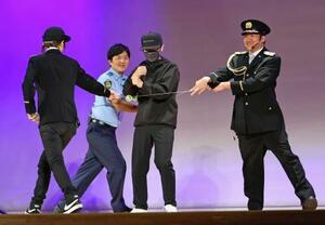 特殊詐欺の犯人役(左から3人目)をヨーヨーの糸を使って取り押さえるパフォーマーら=5日午後、東京都昭島市