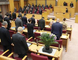 市議在職中に死去した志田常佳さんをしのび、黙とうする市議や市幹部ら。議席には花が供えられた＝１７日、新潟市議会