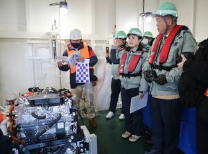 水素燃料発電機について説明する本間組の担当者(中央)=12月25日、新潟市中央区