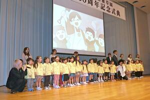 「ひなた」の２人と共に１００周年記念ソングを披露する園児たち＝１６日、長岡市台町２