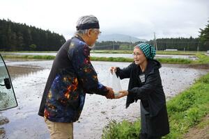 田植えの準備をしている生産者におにぎりを手渡す右近由美子さん=関川村高田