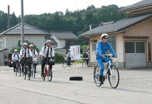 サイクルポリスの先導で自転車を走らせる村上桜ケ丘高野球部員たち=村上市七湊
