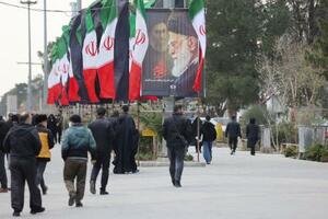 　９日、イラン・テヘランで、国旗や殺害されたハメネイ師のポスターが掲げられた通りを歩く人（ＷＡＮＡ提供・ロイター＝共同）