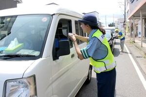 ドライバーに梅干しを手渡して交通事故防止を呼びかける江南署員ら=7月22日、新潟市江南区亀田本町2