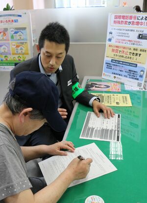 特殊詐欺の被害に遭わないよう、国際電話の着信を休止する申込書に記入する来店客(手前)=加茂市番田