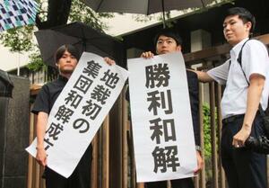 　建設石綿訴訟の和解成立後、「勝利和解」などと書かれた紙を掲げる弁護団＝２６日午後、東京地裁前