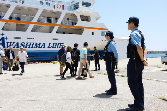 粟島汽船のフェリーから下船する来島者を見守る臨時交番の警察官=11日