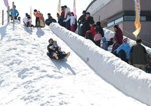 青空の下、白銀の滑り台を楽しむ親子連れ=15日、長岡市千秋3