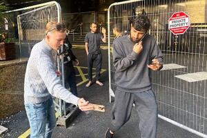 ホテルから出てきた難民申請者(右)にスマートフォンを向けながら質問するエディーさん=10月、ロンドン(共同)