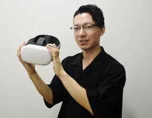 ゴーグル型の仮想現実(VR)装置を手にする梅津円さん=東京都港区