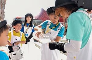 屋外で働くスタッフらにスポーツドリンクをついで回る仕事体験の小学生ら=3日午後、大阪市此花区の夢洲