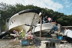 　辺野古沖で転覆した船「平和丸」（左）と「不屈」に花を供える人たち＝３月、沖縄県名護市