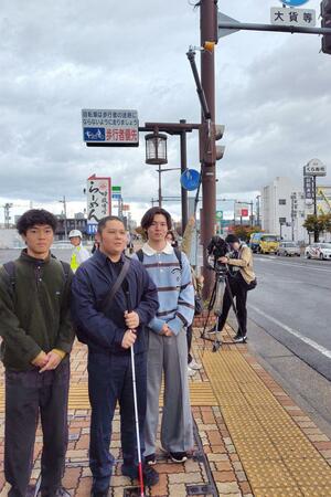 視覚障害者用の音響装置が新設された横断歩道の信号機。県警に設置を訴えた神原聡太さん（中央）＝新潟市中央区紫竹山６