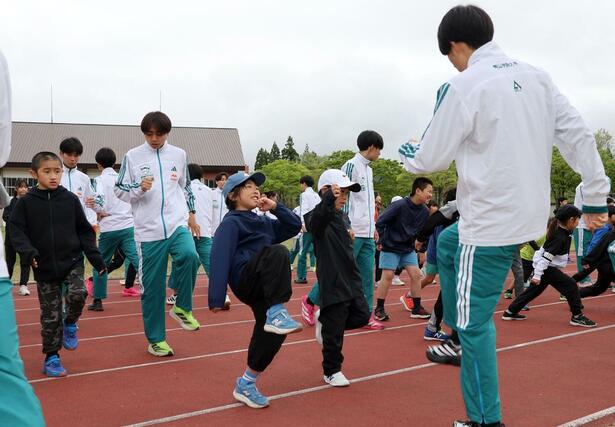 青山学院大陸上競技部員からウオーミングアップの方法を教わる地元の子どもたち＝４日、妙高市関川