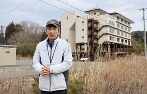 　「たろう観光ホテル」（奥）近くの自宅跡地に立つ小幡実さん＝５日、岩手県宮古市