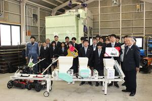 JA共済連県本部が寄贈した乾燥機(中央奥)などの農業機械に囲まれ、記念撮影をする佐渡総合高の生徒ら=新潟県佐渡市栗野江