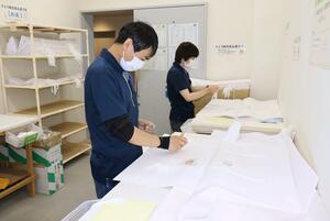 着物を包む「たとう紙」のひも付け作業をする知的障害者の男性ら=十日町市のきものブレイン