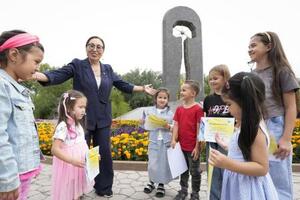 「この国の被ばくの歴史を忘れないで」と子どもたちに語りかけるアベノバ(左から3人目)。後ろには核爆発からわが子を守る母親の像「死よりも強し」が見える=2025年8月、カザフスタン・セメイ(撮影・小崎一記、共同)