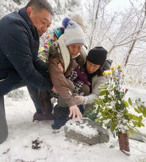 父親の神庭利太さんが眠る墓石に手を触れるロサリナ・カンバ・フェルナンデスさん(中央)=30日午前、鳥取県伯耆町