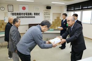 防犯機能付き電話機を市民に手渡すエコー金属の田野隆夫社長(右)=燕署