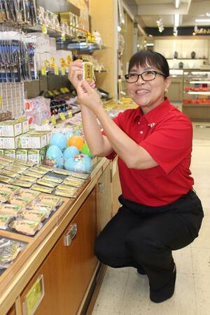 職場である売店で、外国人に人気の小判形マグネットを手にする田辺カロリーナさん=佐渡市相川地区