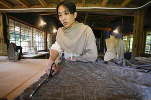 自宅敷地にあるアトリエで布を裁断する居相大輝。「僕が作る服はモードというより、大切な人のために家庭で縫われてきたものに近い」=2025年4月、兵庫県朝来市(撮影・林昌三)