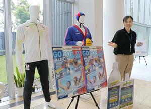 ブルボン本社の玄関に飾られた代表のユニホームなどを紹介する東京五輪水球女子日本代表の小出未来さん=柏崎市