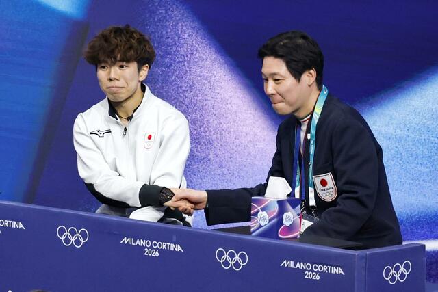 男子フリーの得点を確認し日下匡力コーチ（右）と握手する佐藤駿＝ミラノ（共同）