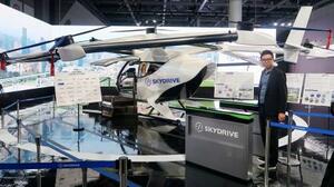 スカイドライブがジャパンモビリティショーで展示する、空飛ぶクルマの模型と自動改札機。右は福沢知浩CEO=29日午前、東京都江東区の東京ビッグサイト
