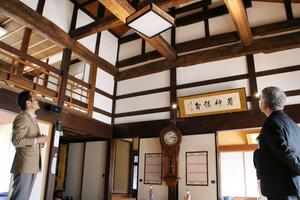 天井が高く、太いはりが巡らされた杉原家住宅の広間。左は登録証授与式の出席者を案内する杉原泰洋さん=新発田市上赤谷