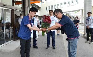津南病院に赴任した佐藤恵介さん（左）にシャクヤクの花束を手渡す中澤寛人組合長＝津南町下船渡