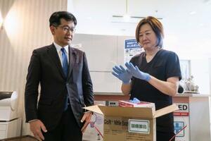 　配送された国備蓄の医療用手袋を着ける「天王洲パークサイドビル歯科」の坂田香里院長。左は厚労省の仁木博文副大臣＝２３日午後、東京都品川区
