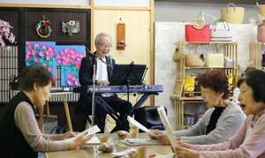 「うたごえ広場」を訪れた人々と、伸びやかに歌う永田宏行さん(奥)。楽しいトークも交え、笑顔の輪が広がった=加茂市穀町の「かも小町」