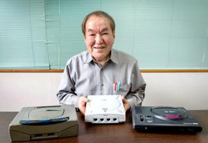 セガ元社長の佐藤秀樹さんと、家庭用ゲーム機(同社提供)