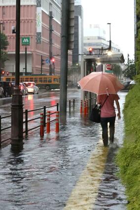 早朝から降り続いた雨で新潟日報メディアシップ前の歩道は水に漬かった。傘や雨具で雨よけをした市民が足早に目的地へと急いでいた＝７月２５日、新潟市中央区万代３