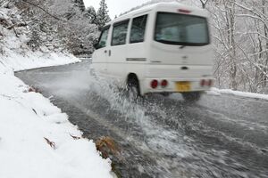 雪を溶かすために水を流している国道405号。車が水しぶきを上げ、行き交う=津南町大赤沢