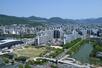 南側から望む基町地区。「くの字」の形をした高層アパート群(中央)の後ろを旧太田川(本川)が流れる。左手前は「ひろしまスタジアムパーク」のエディオンピースウイング広島や芝生広場。右手前は広島城=2025年5月