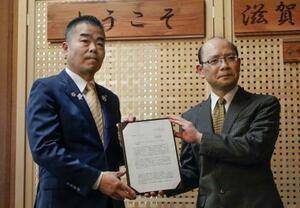 　滋賀県税制審議会から中間答申を受け取る三日月大造知事（左）＝４日午後、滋賀県庁