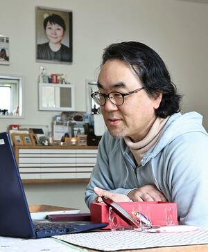 自宅で県議会のインターネット中継を見守る橋本雄一郎さん。奥に飾られている写真は妻桂子さん=18日、上越市