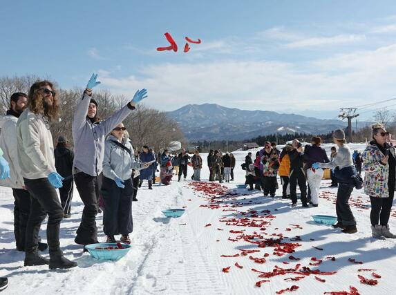 好天の中、トウガラシを雪に投げる外国人観光客ら=20日、妙高市