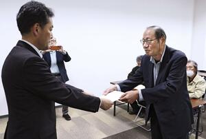 青森県むつ市の担当者(左)に中間貯蔵施設への使用済み核燃料搬入計画に反対する申し入れ書を手渡す市民団体の男性=4月25日、むつ市役所