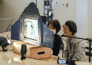 平和活動40年のパネル展に合わせ、紙芝居を披露する三田村静子さん(右)=16日午後、長崎市