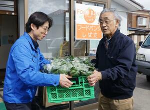 JA北新潟農産物直売所「こったま〜や」の窪田一成店長(左)からホウレンソウを受け取ったフードバンクしばたの土田雅穂副代表=新発田市本町3